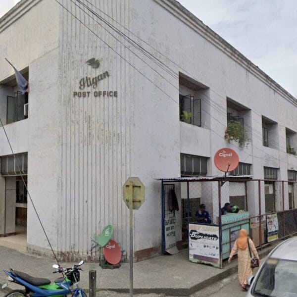 baguios post office building, philippines, with motorcycles and cars parked outside on a cloudy day.